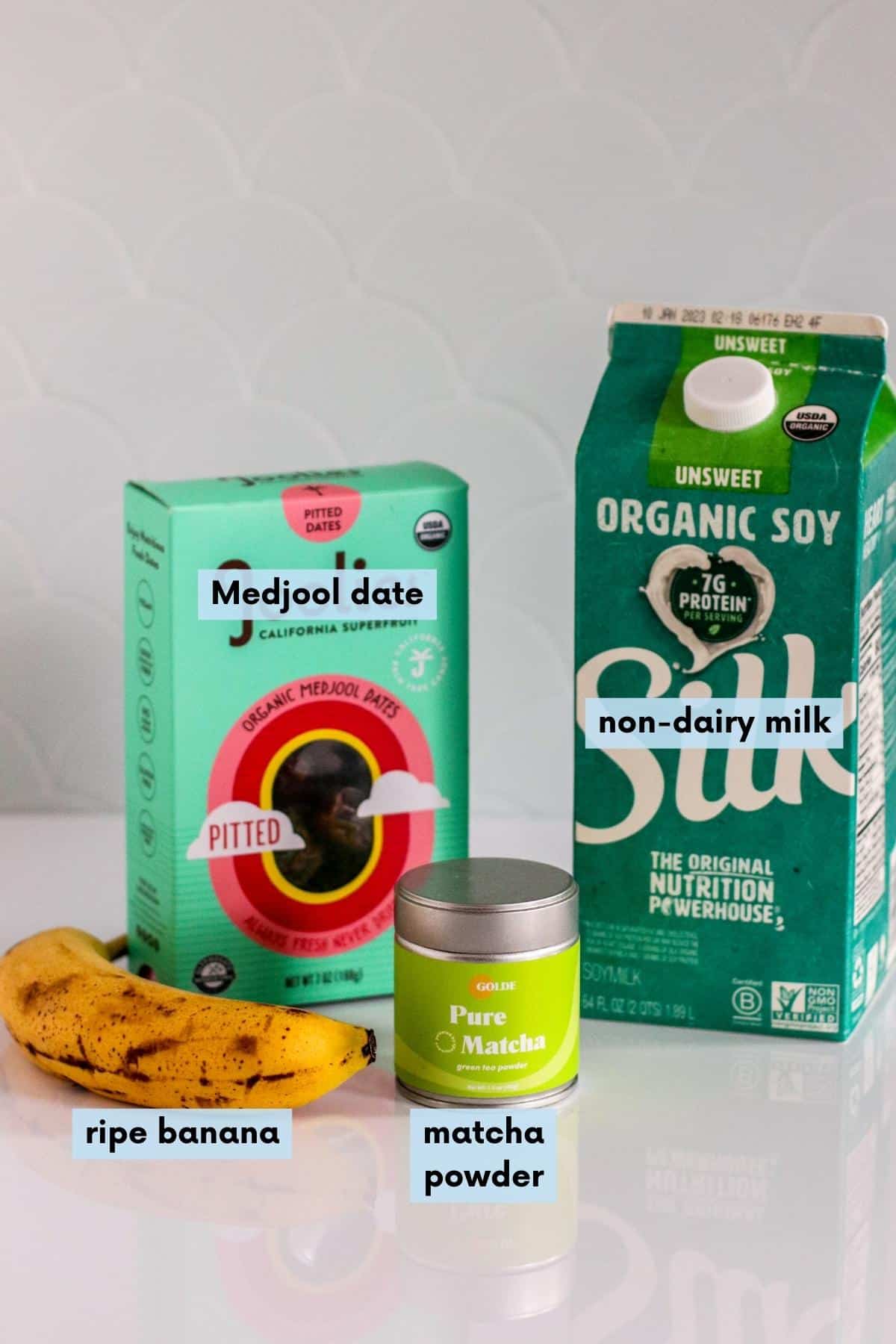 Ripe banana, box of Medjool dates, container of matcha powder, and a carton of soy milk.