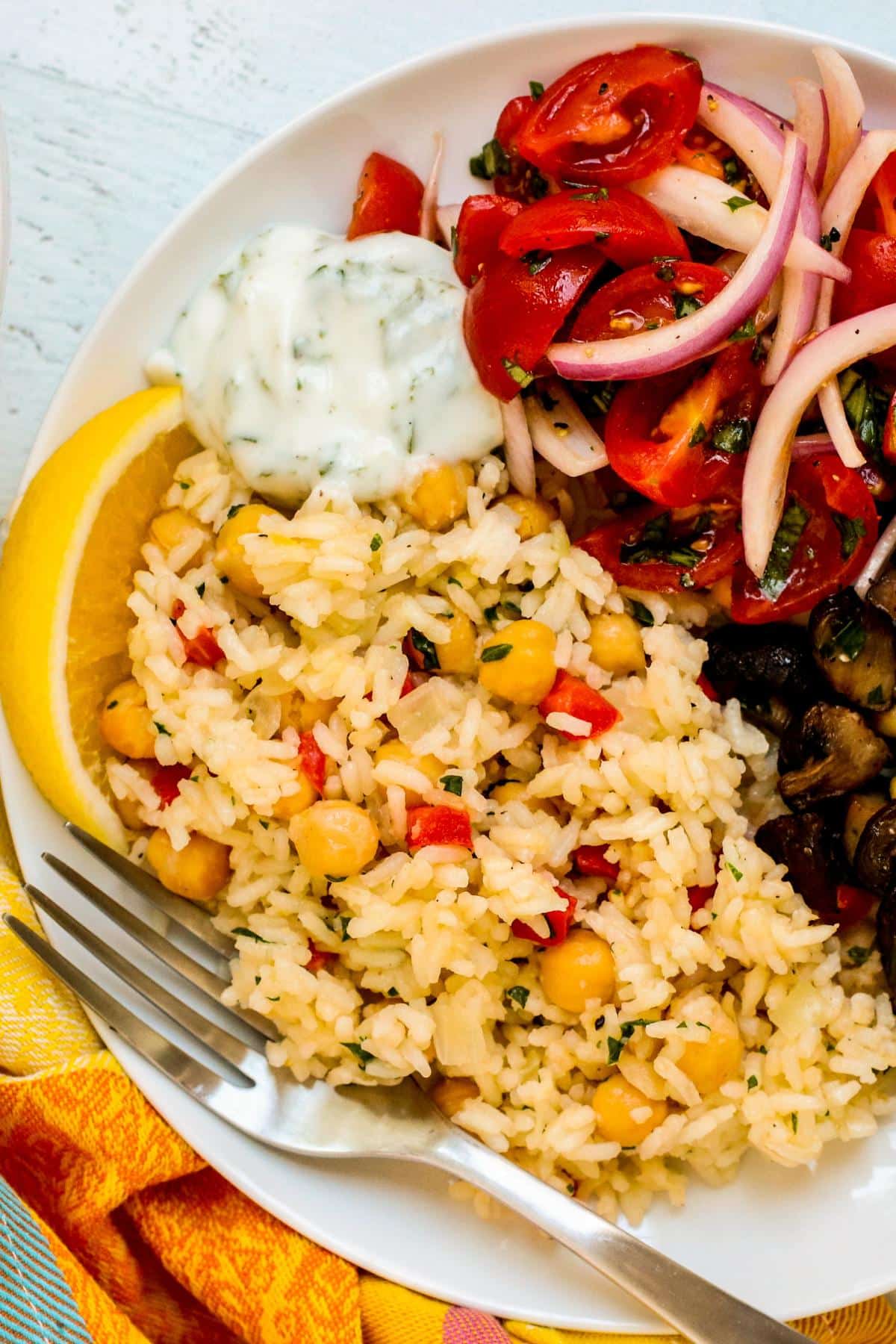 Dollop of yogurt sauce on a plate with chickpea rice pilaf, tomato and onion salad, and roasted mushrooms.