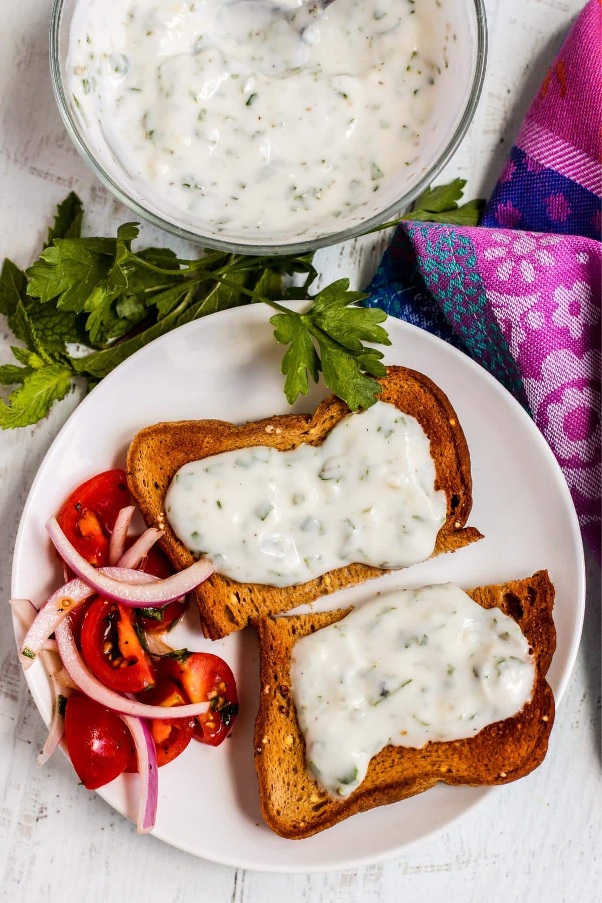 Whole grain toast topped with yogurt sauce and a side of tomato and red onion salad.