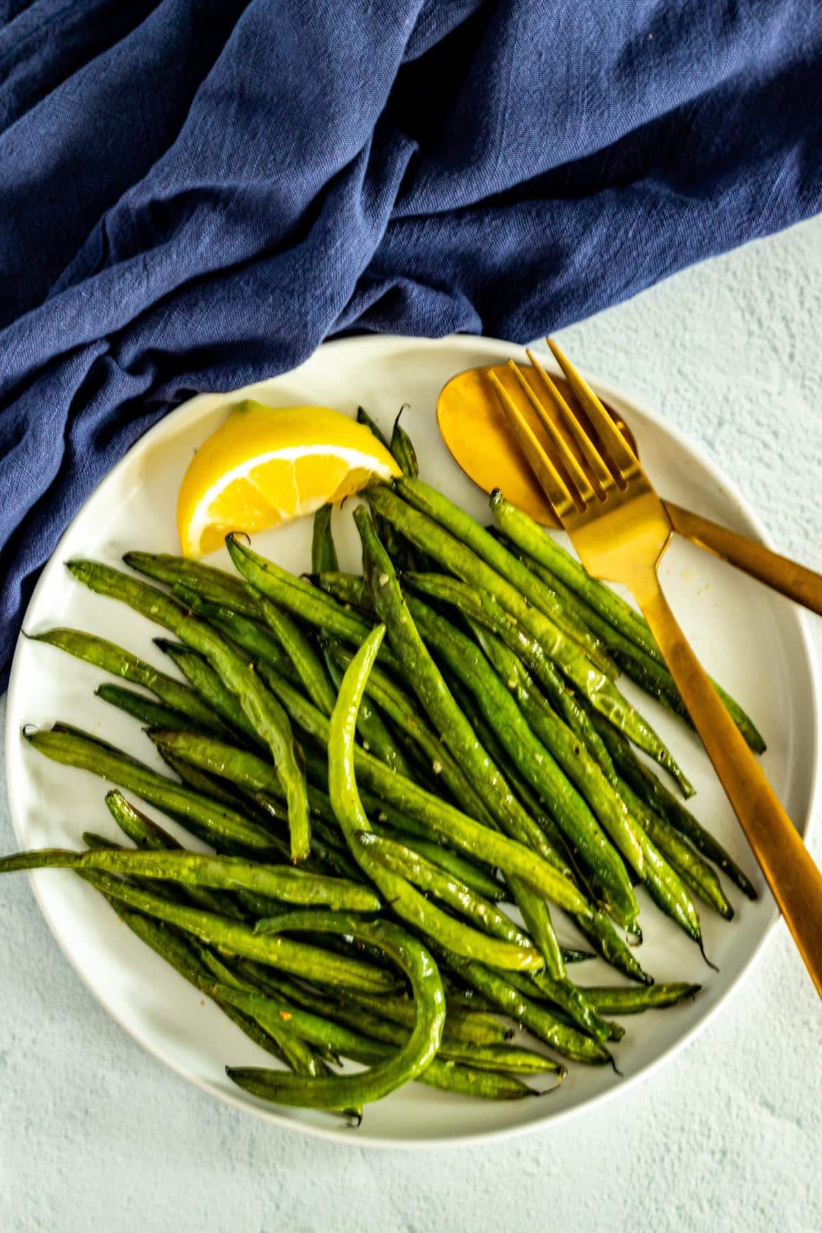 Plate of green beans with serving utensils and lemon wedge.