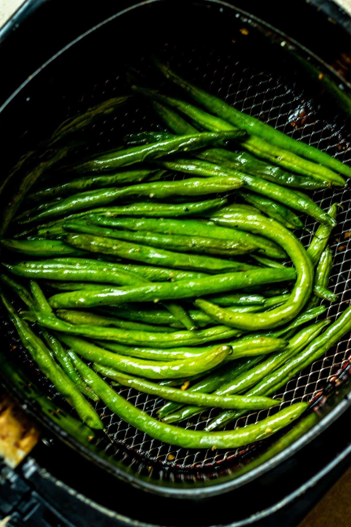 Cooked green beans in an air fryer basket.