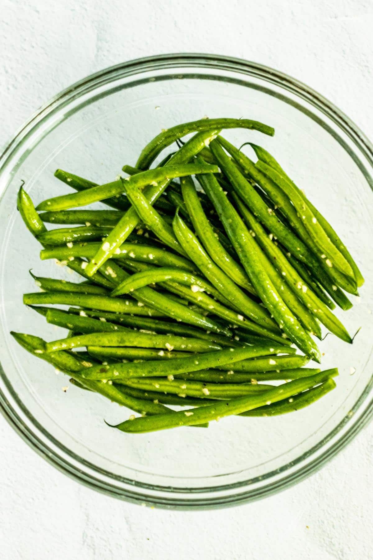 Green beans and garlic in a mixing bowl tossed with olive oil and salt and pepper.