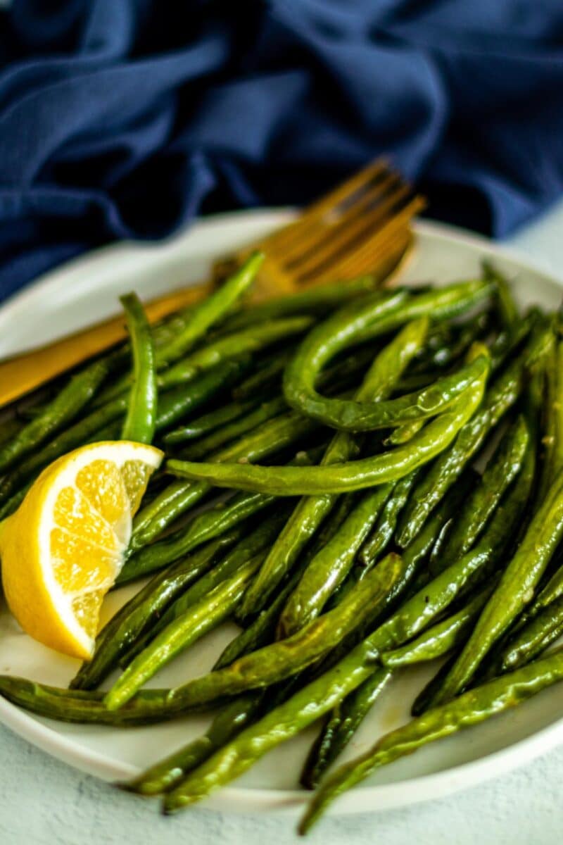 Air fryer green beans and a lemon wedge on a serving platter.