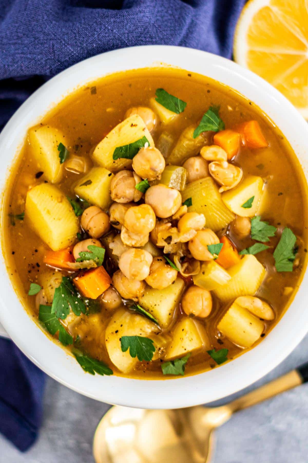 Bowl of chickpea soup with a spoon and lemon wedge next to it.