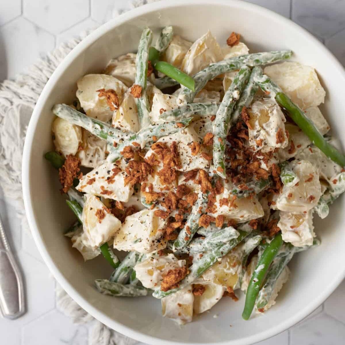 Bowl of creamy potato salad with green beans and vegan bacon crumbles.