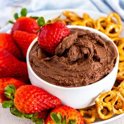 Bowl of chocolate hummus on a platter with strawberries and mini pretzels.