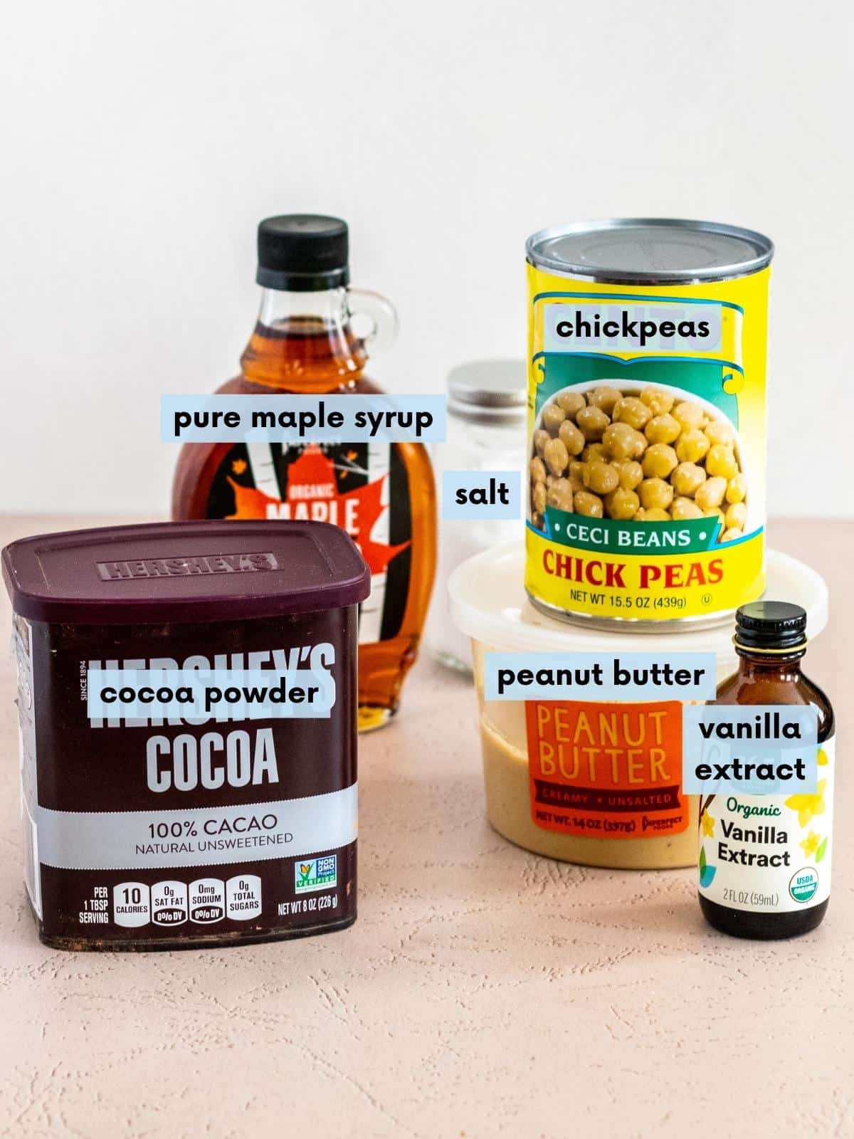 Container of cocoa powder, bottle of pure maple syrup, salt, can of chickpeas, tub of peanut butter, and bottle of vanilla extract.
