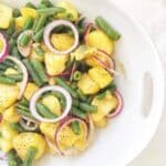 Italian potato salad with green beans and red onions in a serving dish.