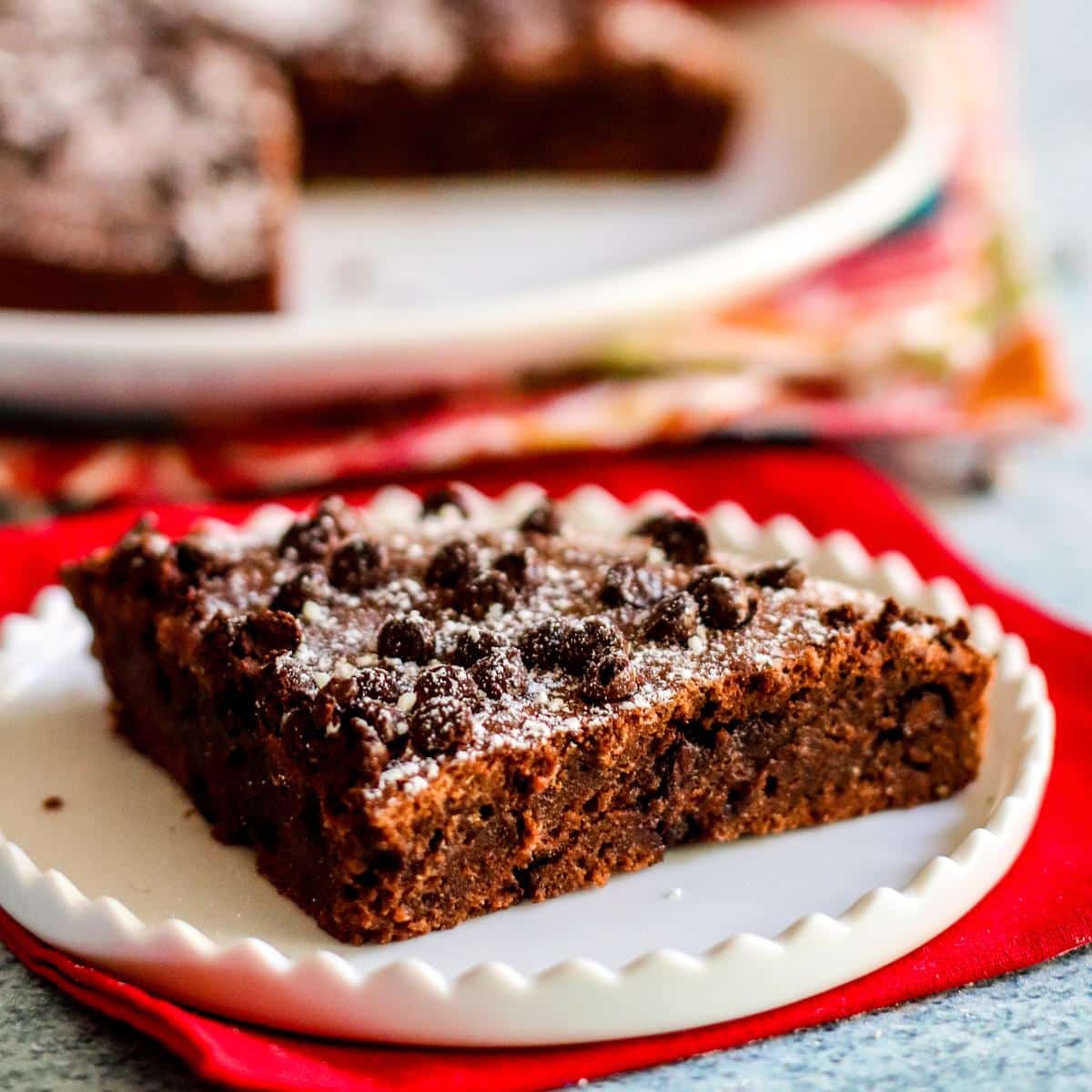 Brownie on a plate topped with powdered sugar and mini chocolate chips.