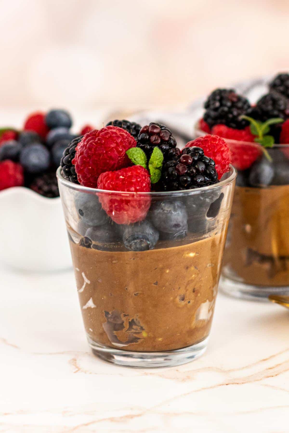 Chocolate mousse in a glass jar topped with blueberries, blackberries, raspberries, and a sprig of mint.