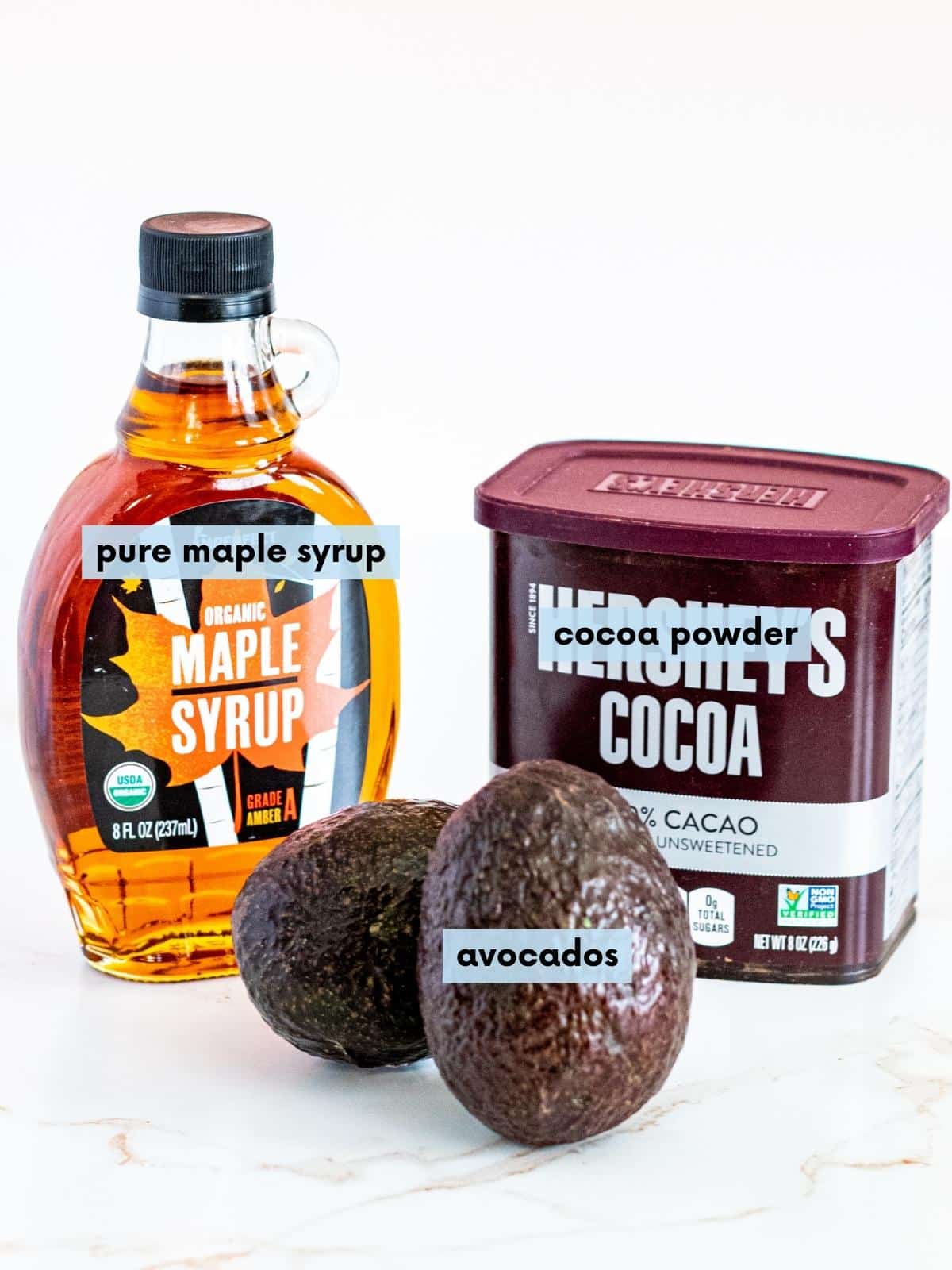 Avocados, bottle of pure maple syrup, and a container of cocoa powder.