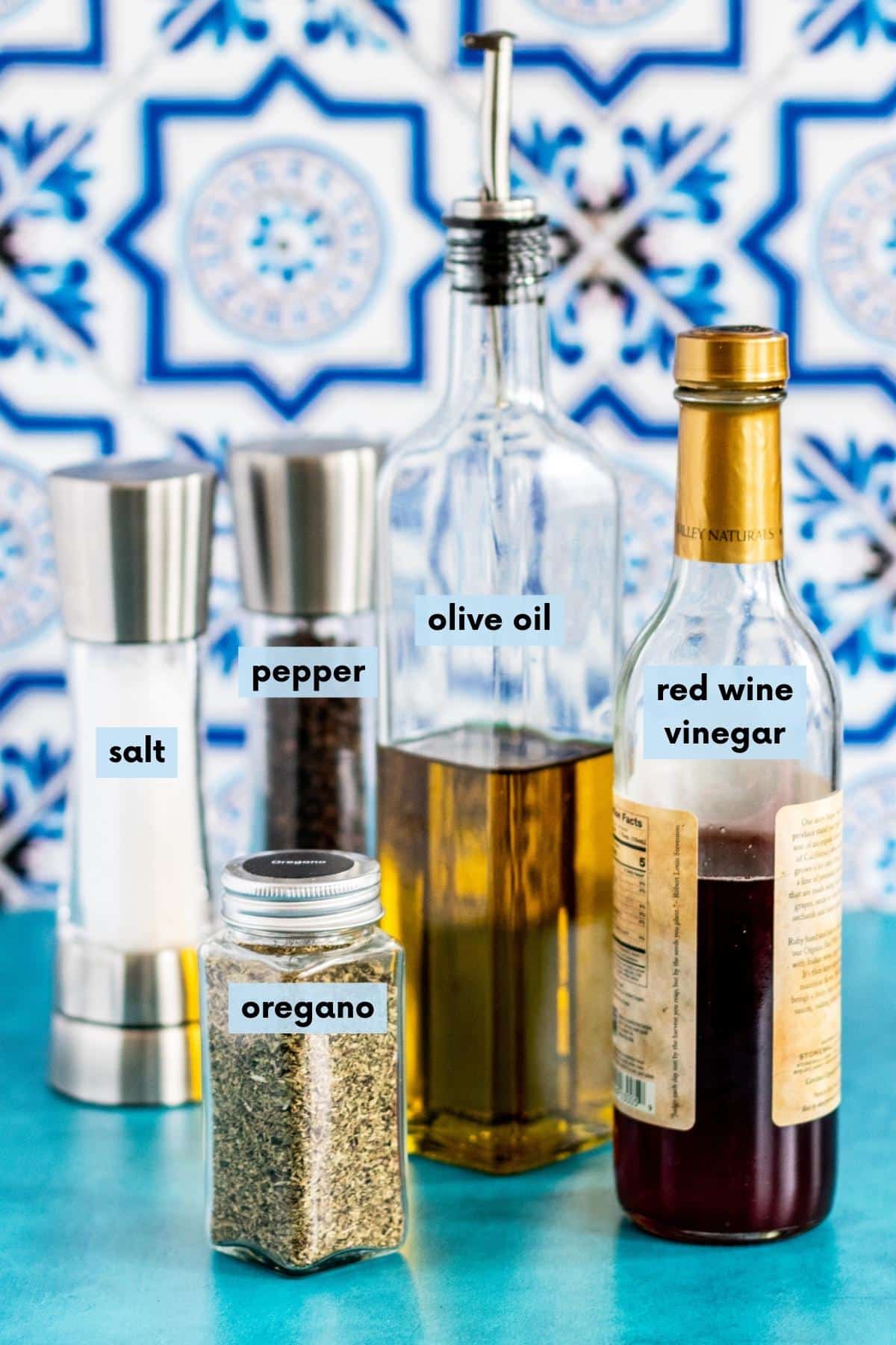 Jar of dried oregano, bottles of olive oil and red wine vinegar, and salt and pepper shakers.