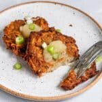 Fork cutting latkes topped with apple sauce and green onions.