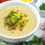 Bowl of baked potato soup topped with vegan cheese shreds, chives, and tempeh bacon.