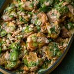 Platter of smashed potatoes drizzled with sauce and topped with sliced green onions and peppers.