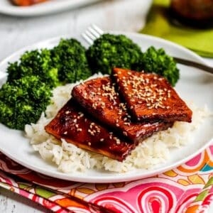 Slices of baked teriyaki tofu topped with sesame seeds on a bed of rice with steamed broccoli next to it.