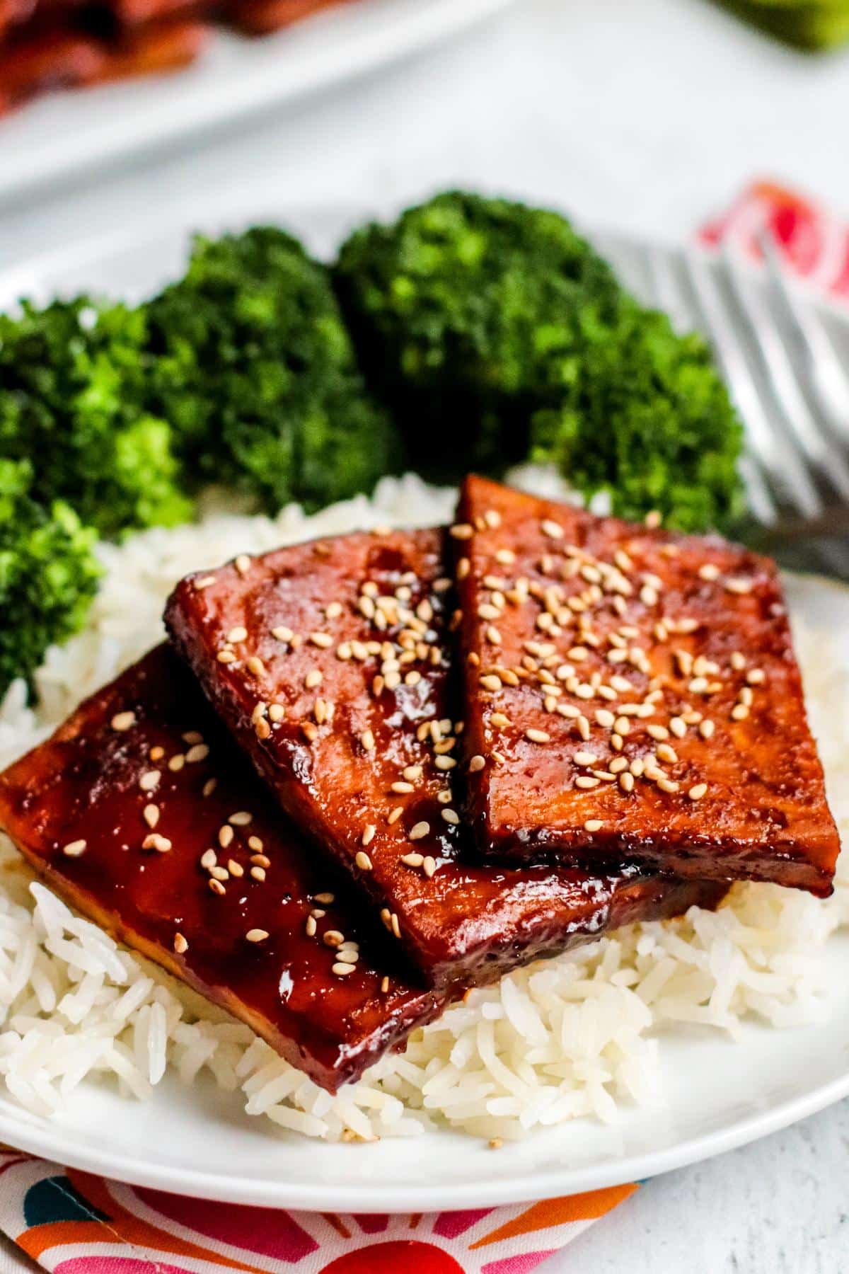 Slices of tofu garnished with sesame seeds on a plate of rice.