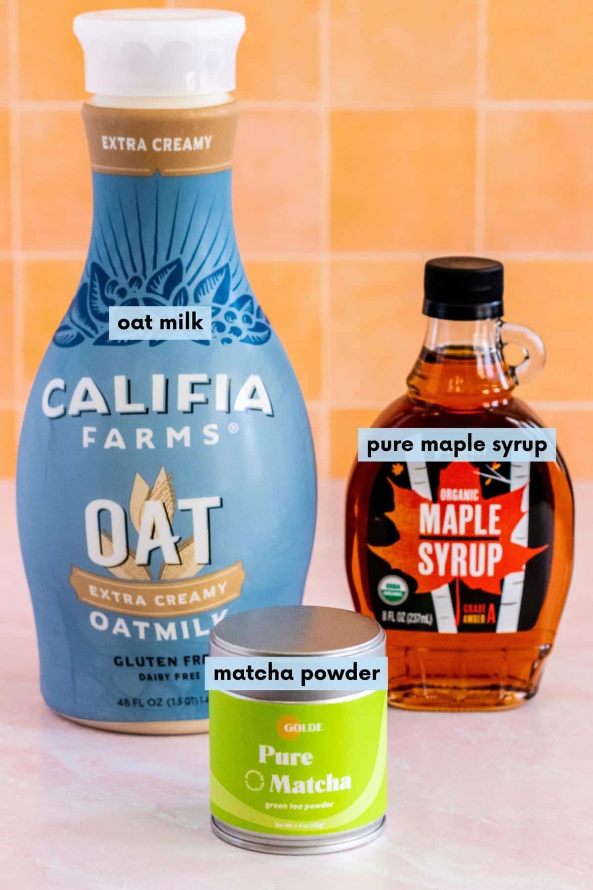 Tin of matcha powder, bottle of oat milk, and bottle of pure maple syrup.
