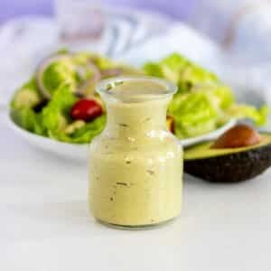 Dressing in a bottle in front of a plate of salad and half an avocado.