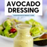 Dressing in a bottle in front of a plate of salad and half an avocado with text overlay Oil-Free Vegan Avocado Dressing.