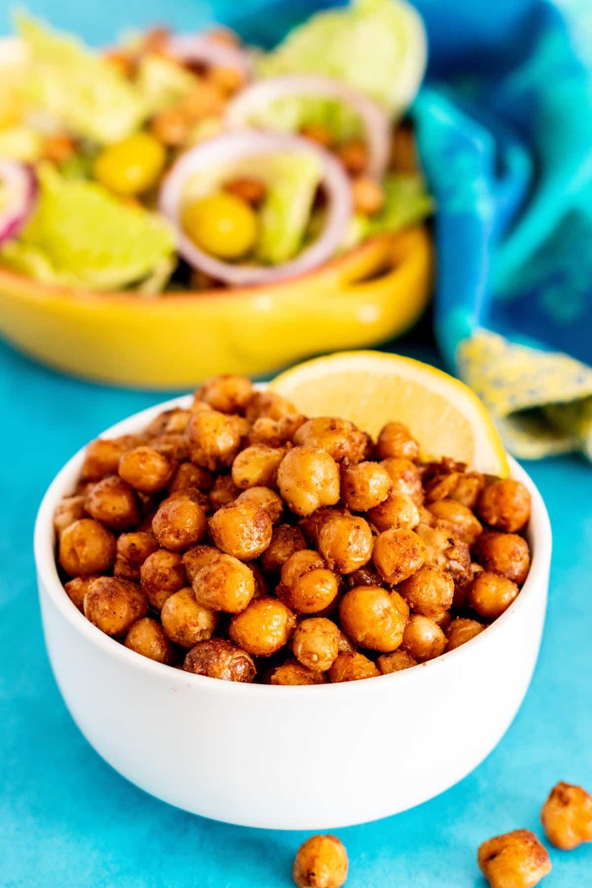 Bowl of pan fried chickpeas with a lemon wedge with a bowl of salad in the background.