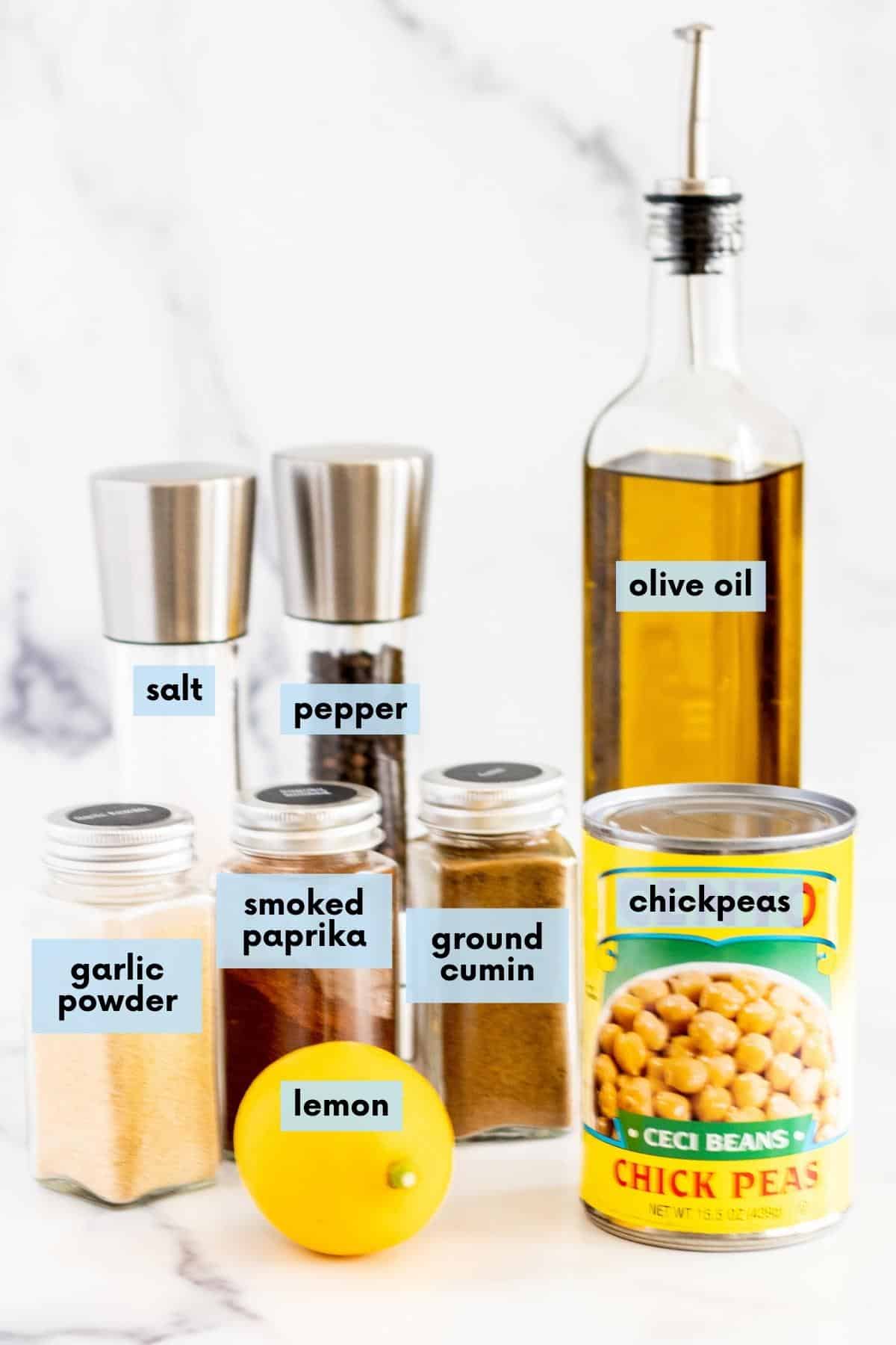 Jars of garlic powder, smoked paprika, and ground cumin, salt and pepper shakers, a lemon, a can of chickpeas, and a bottle of olive oil.