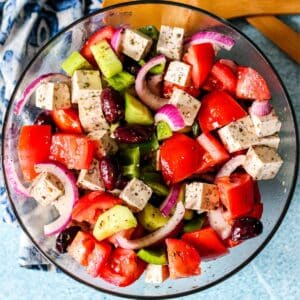 Serving bowl of Greek salad with tomatoes, cucumbers, red onions, green bell pepper, Kalamata olives, and tofu feta.