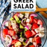 Serving bowl of salad with text overlay Vegan Greek Salad.