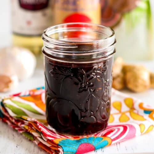 Vegan Teriyaki Sauce in a glass jar on a floral napkin with ingredients in the background.