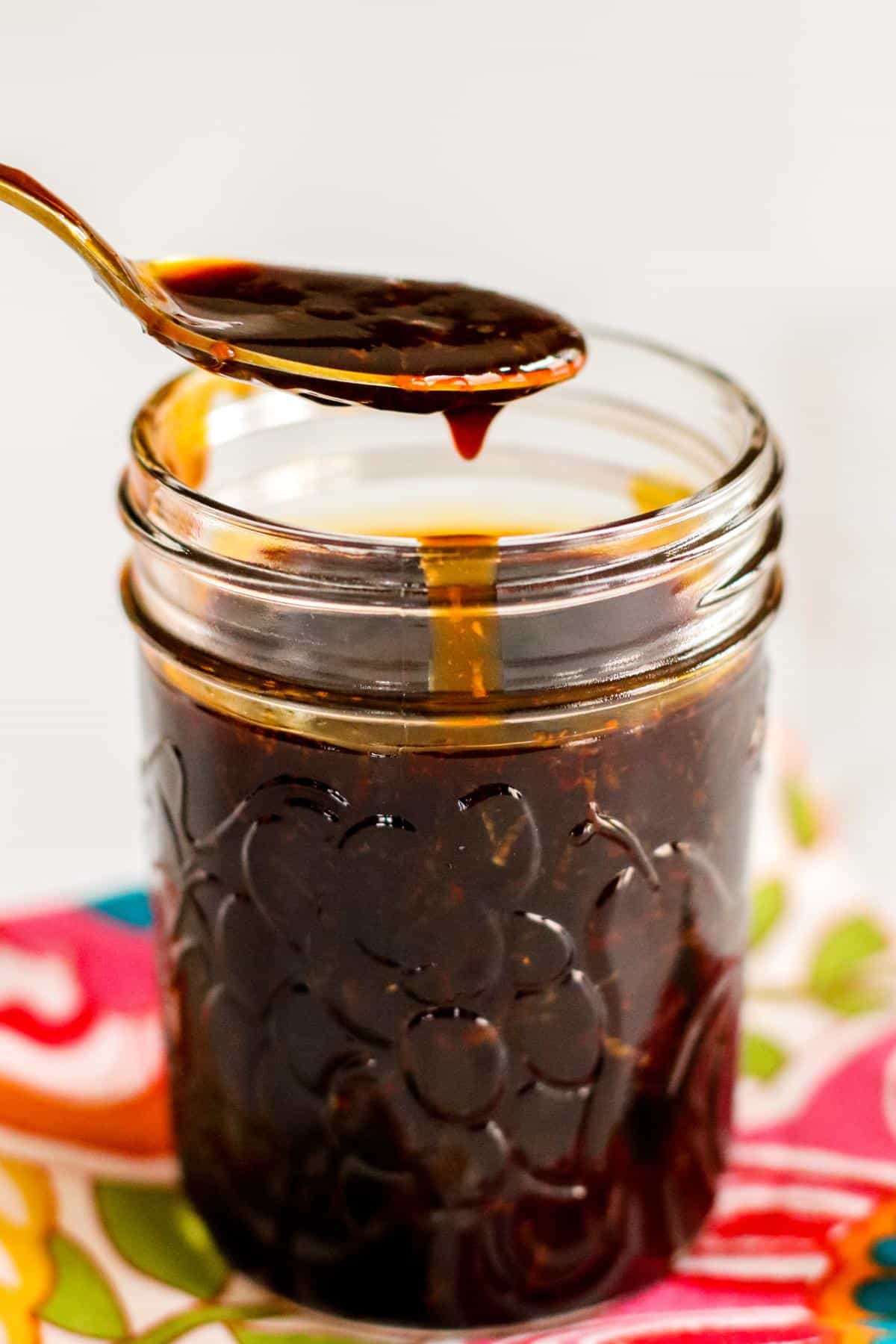 A spoon of teriyaki sauce over a jar of sauce.