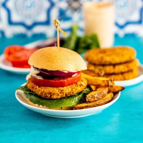 Chickpea burger on a plate with fries and a stack of patties in the background.
