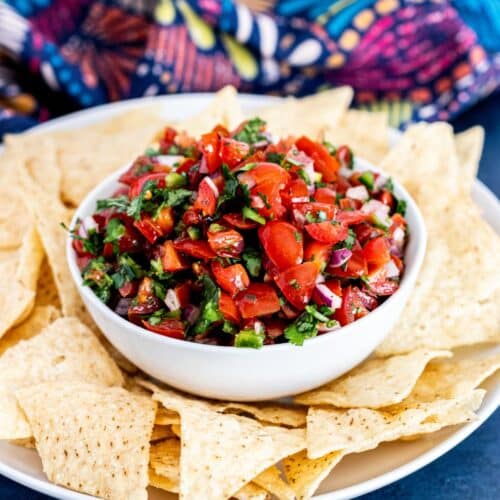 Bowl of cherry tomato salsa on a plate with tortilla chips.