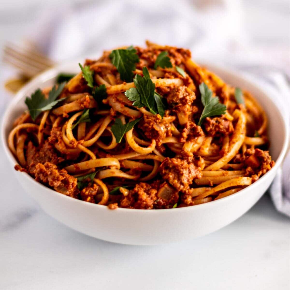 Bowl of spaghetti with vegan bolognese sauce garnished with fresh parsley.