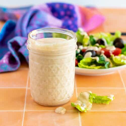 Jar of dressing next to a salad topped with the dressing.