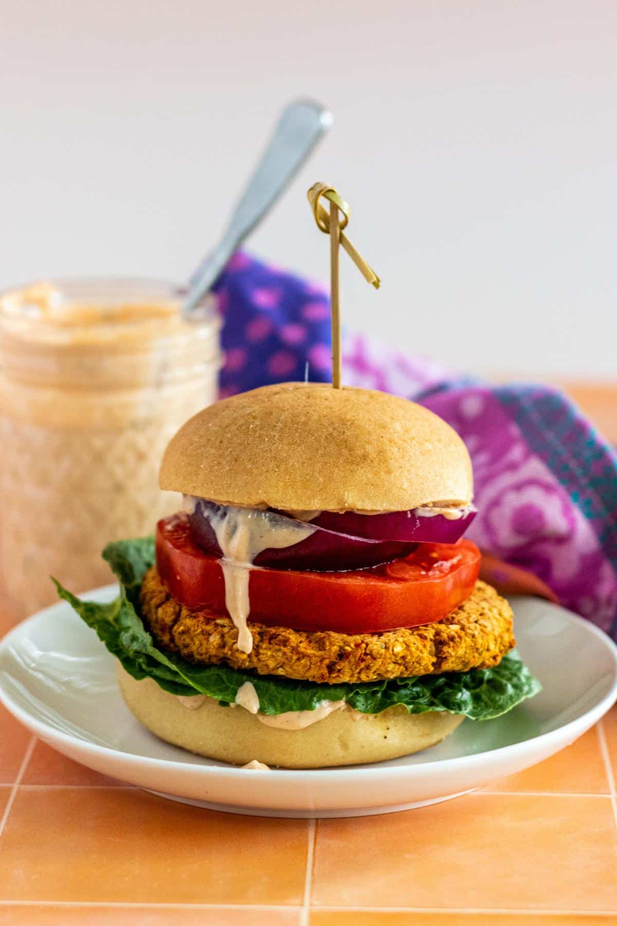 Veggie burger on a bun with dressing dripping down the side and a jar of dressing in the background.