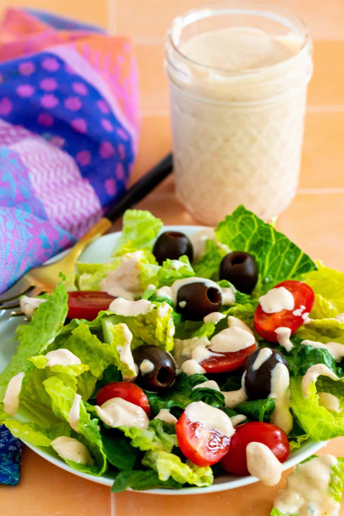 Plate of salad drizzled with dressing and jar of dressing behind it.