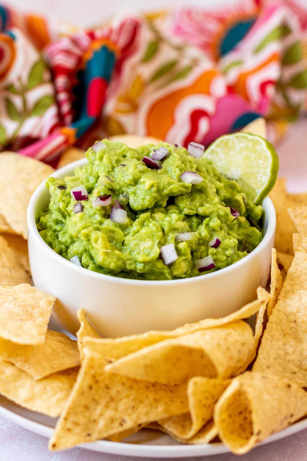 Platter of tortilla chips with a bowl of guacamole in the center garnished with a slice of lime.