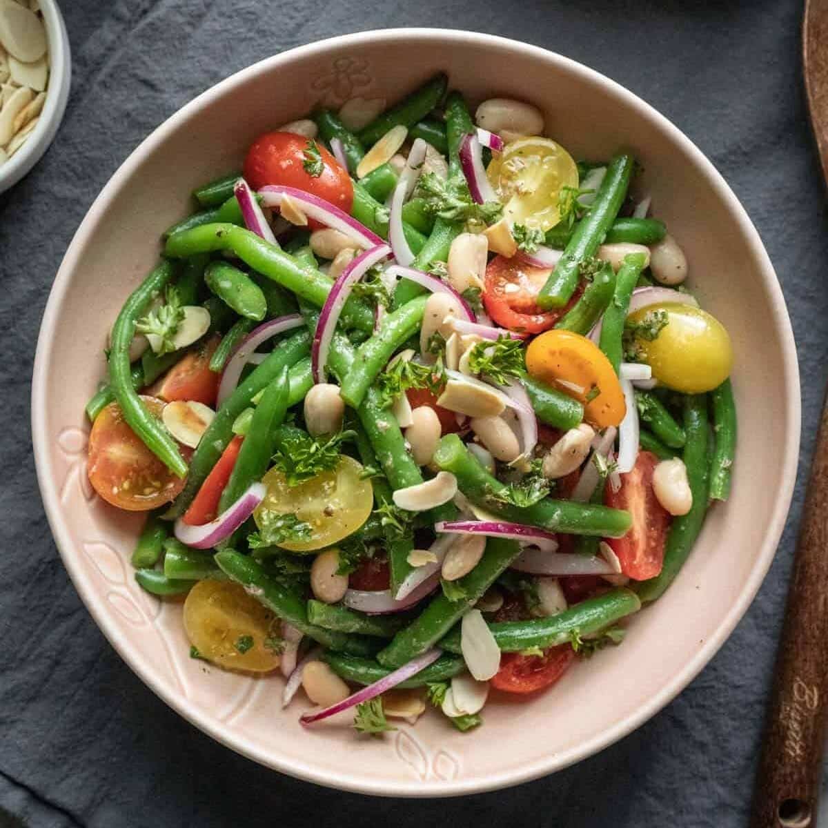 Bowl of salad with green beans, onion, tomatoes, and cannellini beans.