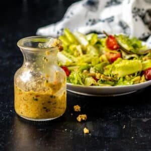 Bottle of green olive dressing in front of a salad tossed with the dressing.