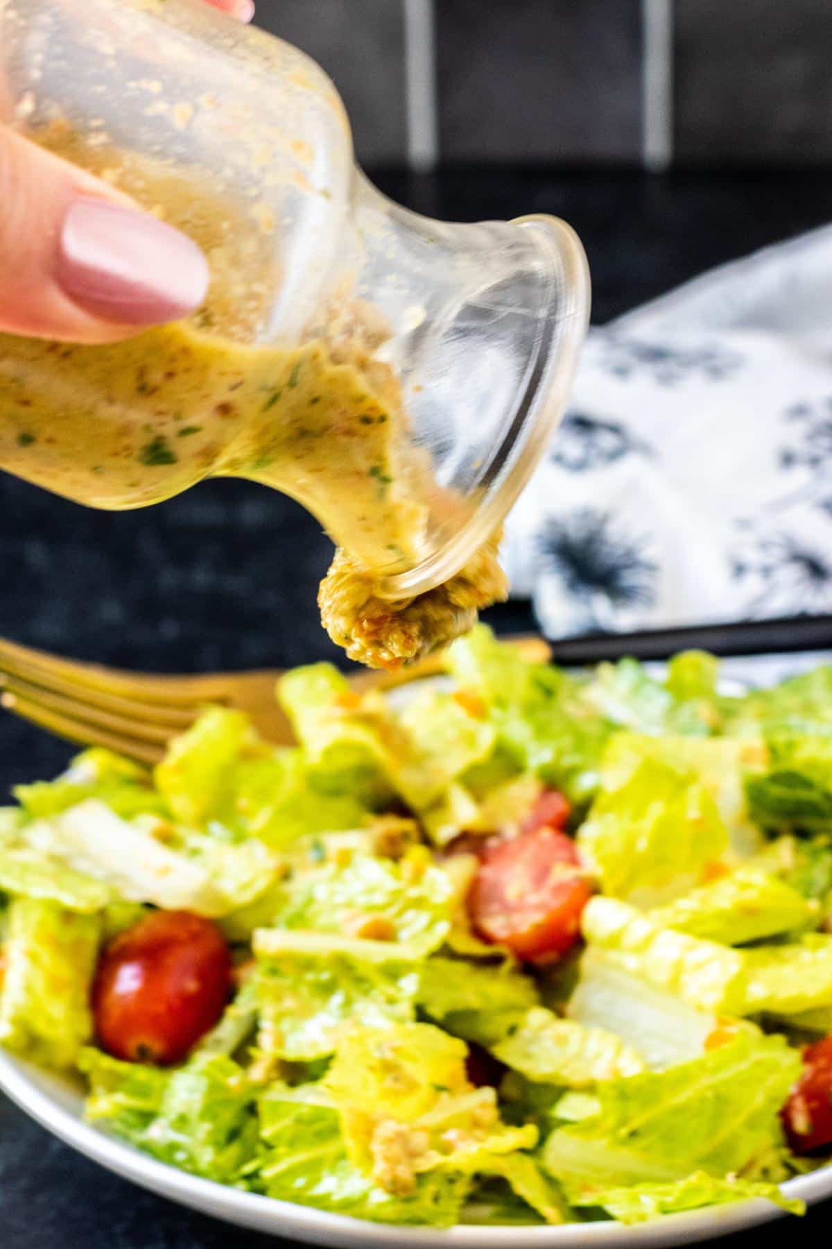 Hand pouring dressing from a bottle onto a salad with lettuce and tomatoes.