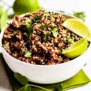 Bowl of quinoa garnishes with lime wedges and fresh cilantro leaves.
