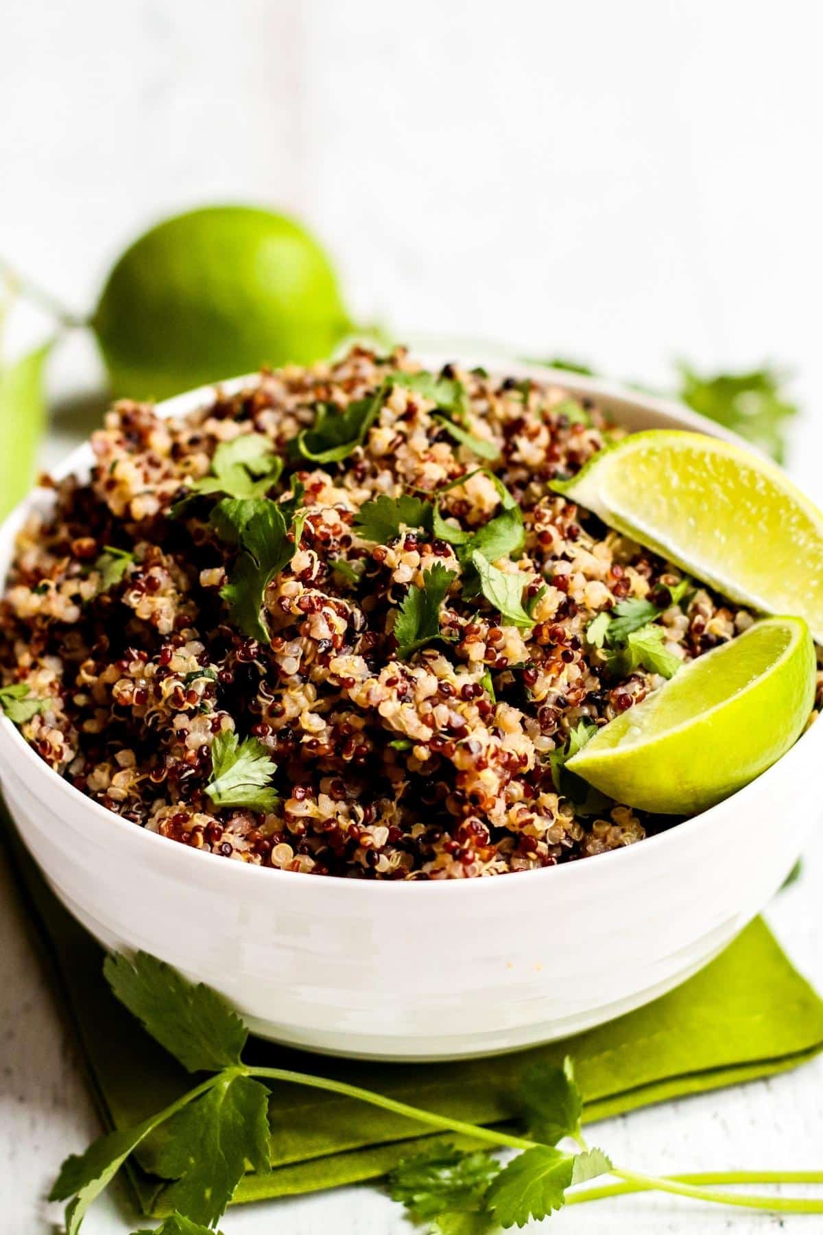 Cooked quinoa in a serving bowl garnished with fresh cilantro and lime wedges.