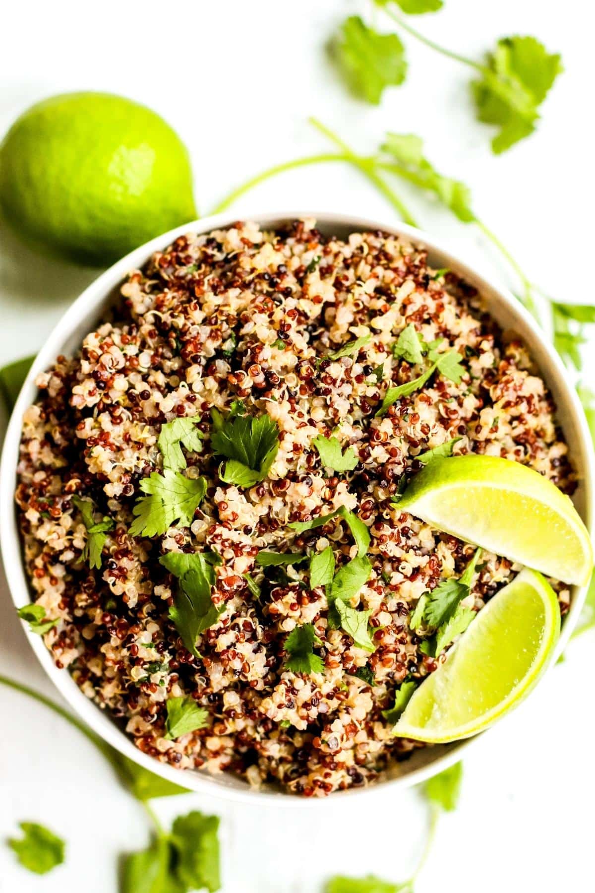 The finished cooked quinoa in a bowl with a lime and stems of fresh cilantro next to it.