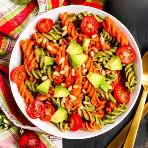 Bowl of red and green pasta topped with cherry tomatoes, avocado, and pine nuts.