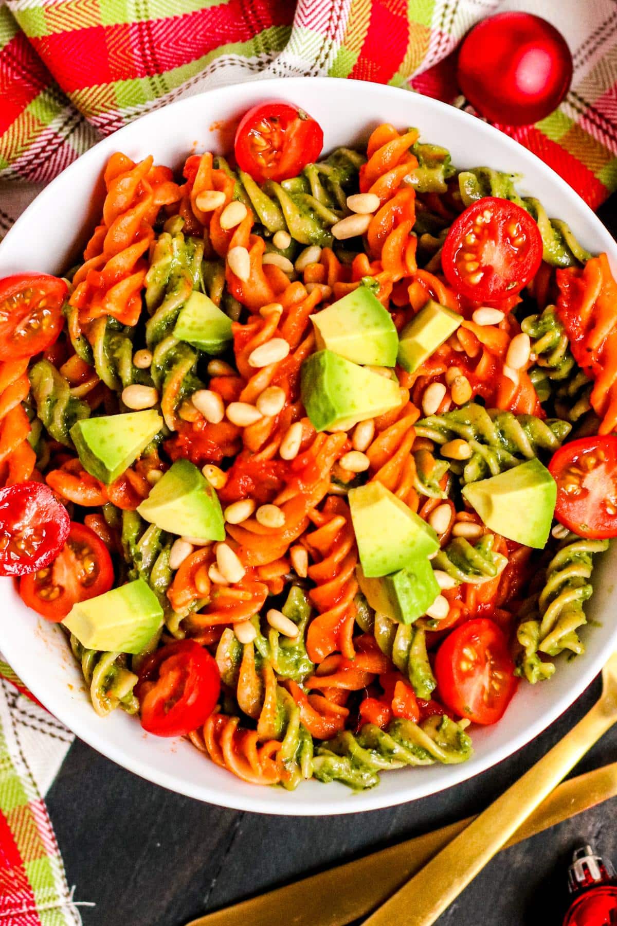 Bowl of Vegan Christmas Pasta topped with cherry tomatoes, avocado, and pine nuts.