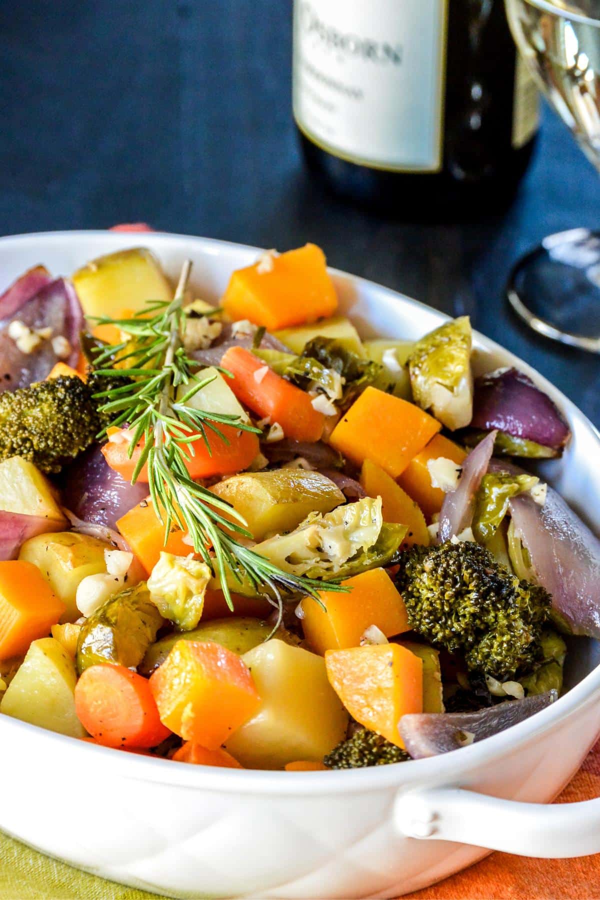 Dish of roasted vegetables next to a bottle of white wine.
