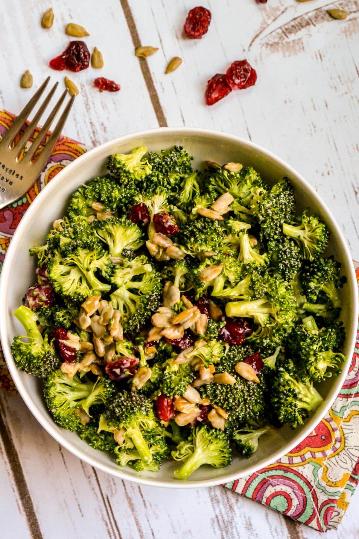 Bowl of broccoli salad with some scattered dried cranberries and sunflower seeds.