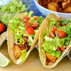 Tacos topped with guacamole, lettuce, and tomatoes.