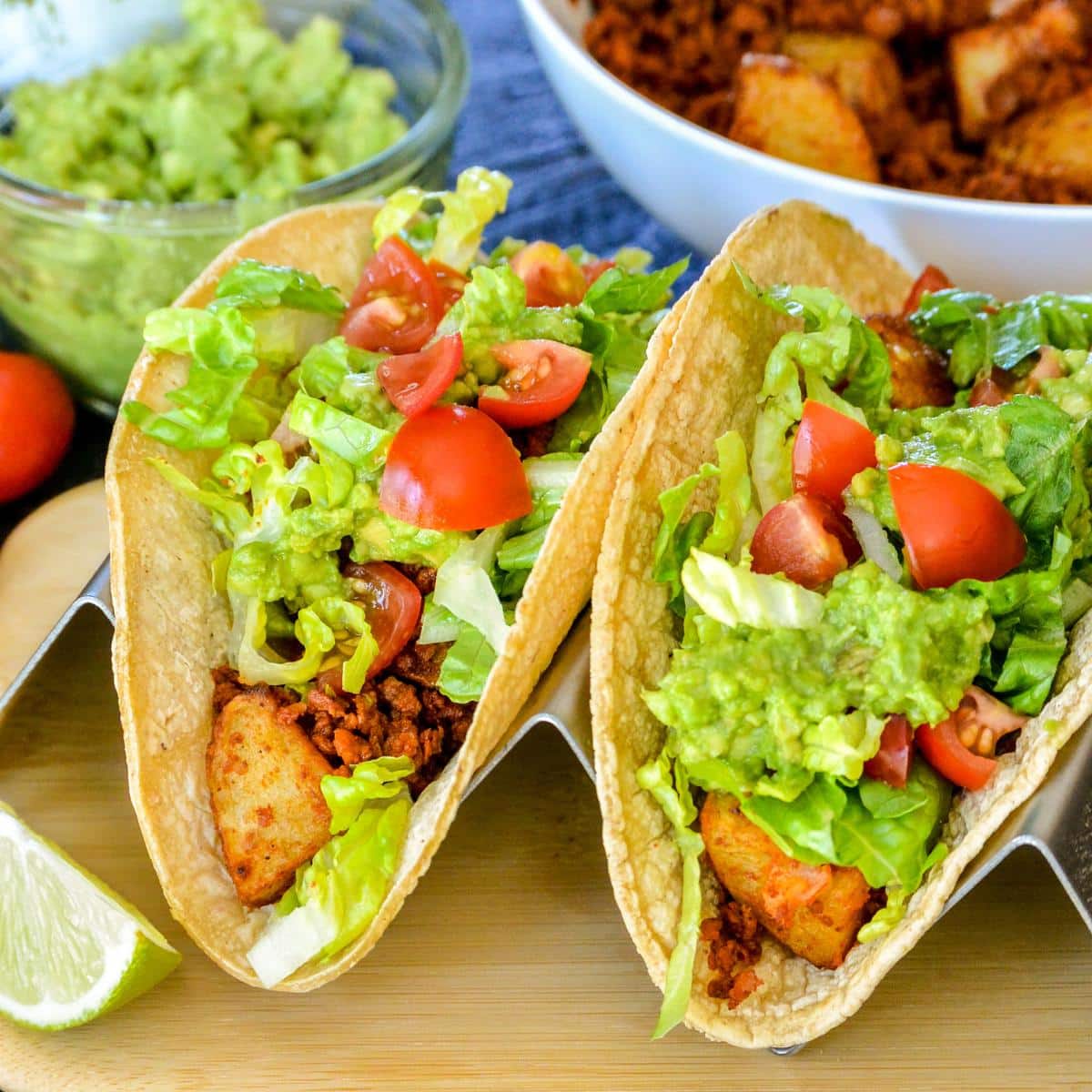 Tacos topped with guacamole, lettuce, and tomatoes.