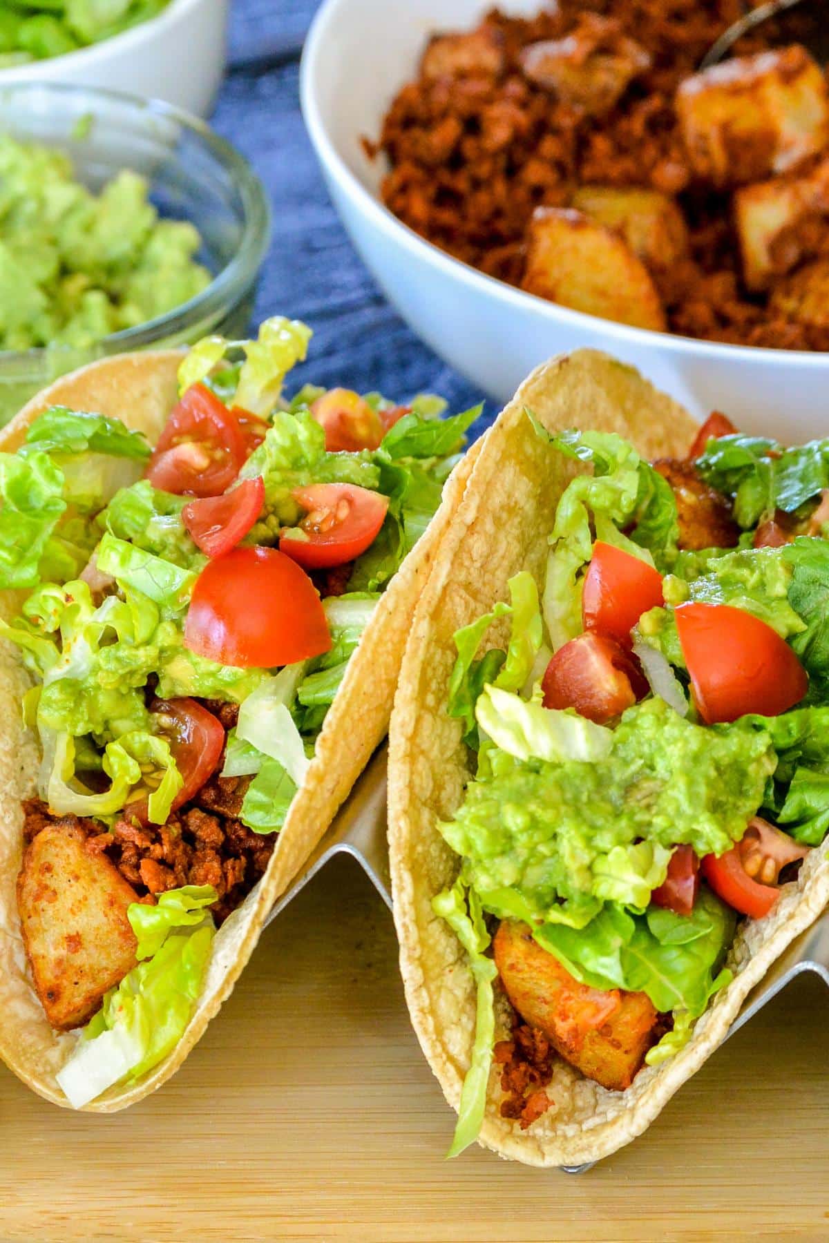 Tacos in front of bowls of soyrizo-potato filling, shredded lettuce, and guacamole.